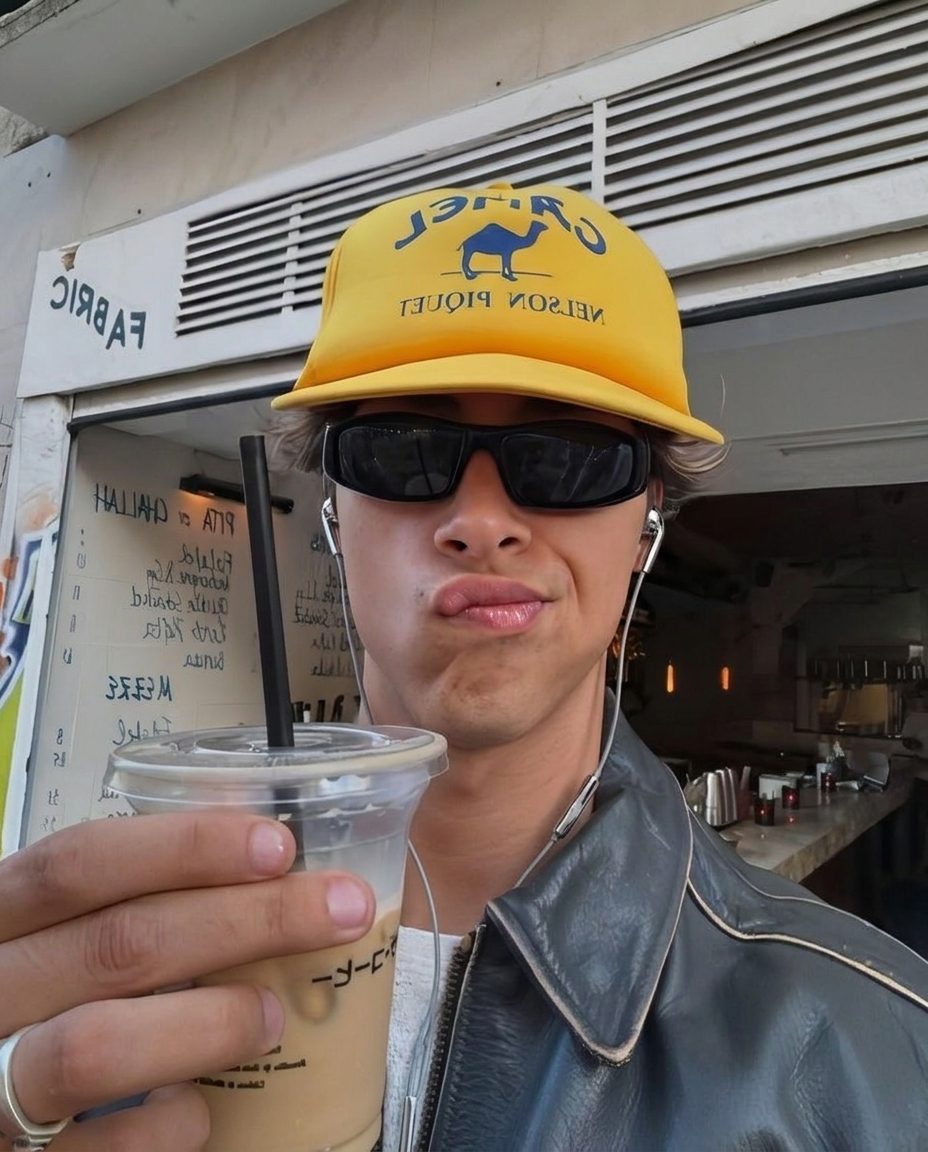 Man in a cap holding an iced coffee, wired earbuds in