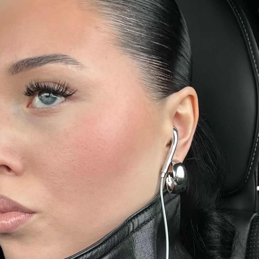 A woman's ear wearing a silver earbud, slicked-back hair and a leather jacket
