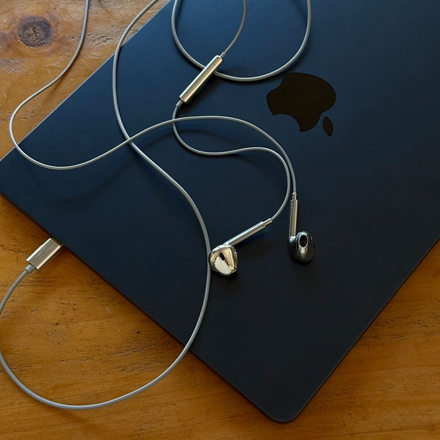Silver earbuds and a USB-C plug on a navy laptop on a wooden desk
