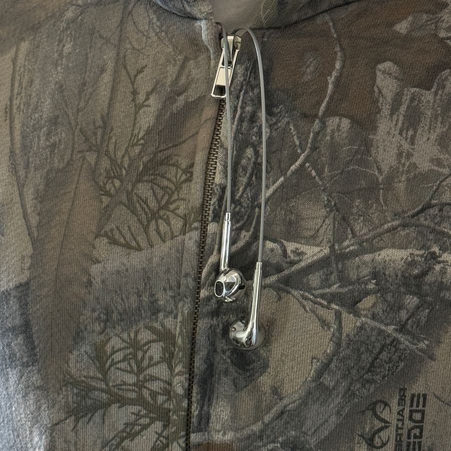 Silver earbuds hanging from the zip of a camo hoodie