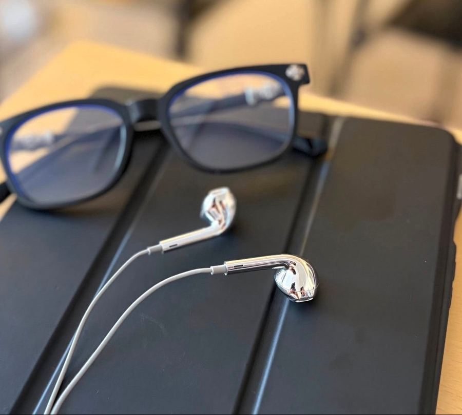 A silver earbud beside glasses on a dark tablet case