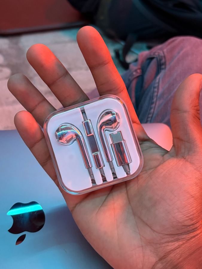 A hand holding the buds in a clear case, a laptop behind